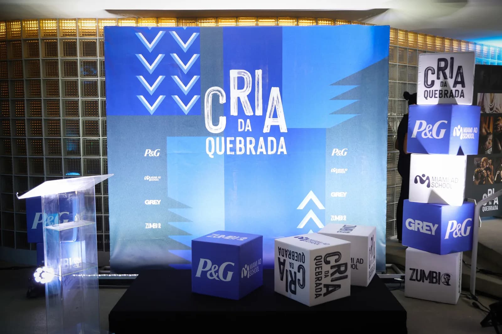 Cenário de fotos da formatura com painel Cria da Quebrada e cubos das marcas parceiras