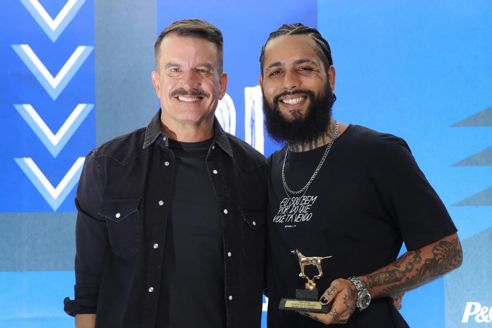 Dois participantes posando com troféu no painel da formatura 2024